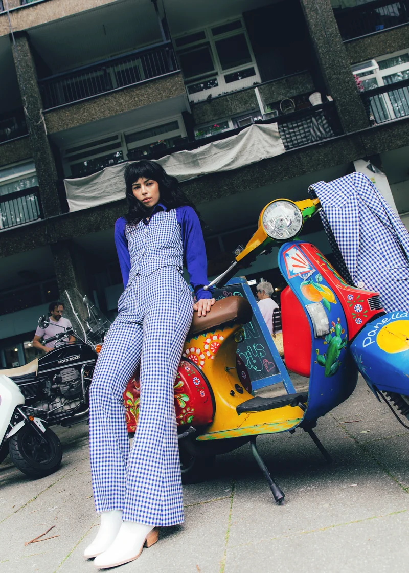 Blue gingham waistcoat and flared trousers beside a vintage scooter